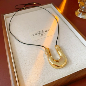 Détail d'un pendentif en métal doré en U avec cordon en cuir noir sur un plateau en lin