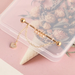 Detailed shot of golden industrial barbell with crystal heart pendant on pink background