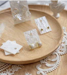Chic earrings displayed on marble cards within a wooden tray with aesthetic props