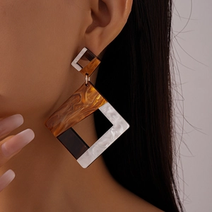 Detail view of large geometric resin earrings with amber and pearl textures on a model