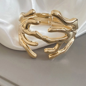 Macro shot of a golden organic hollow-out branch bangle with a sculpted lava texture
