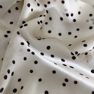 Macro shot of premium cream silk scarf with black polka dots and soft glossy texture