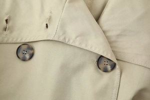 Detailed close-up of khaki trench coat collar with tortoise buttons and twill fabric texture