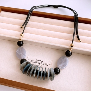 Detail of bohemian necklace with black beads and marble-textured discs on velvet display