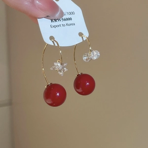 Close-up of asymmetrical gold earrings featuring red resin beads and crystal stars