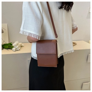 Brown rectangular crossbody phone bag styled with white tassel top and black trousers