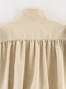 Close-up of the elegant pleated detail and standing collar on this beige woven jacket
