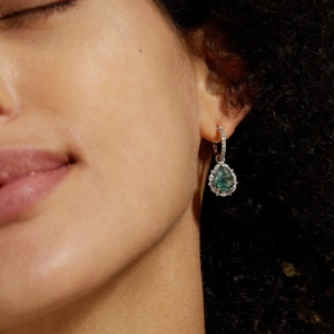 Close-up of pear-shaped moss agate earrings with silver accents and diamond halo on model