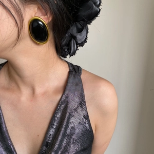 Close-up of vintage black oval earrings with gold metal frame worn by a female model