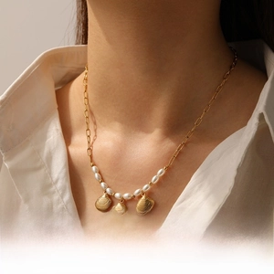 Détail du collier pendentif coquillage doré avec perles porté sur chemisier blanc