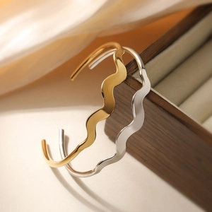 Polished wave-shaped open bracelets in gold and silver finish resting on a wooden box