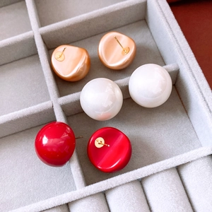 Close-up of minimalist pearl stud earrings in gold, white, and red on velvet tray