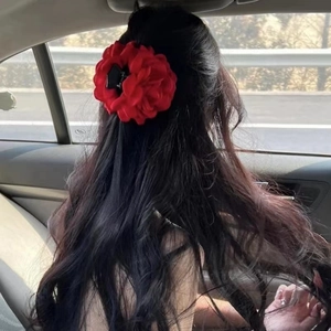 Red fabric flower hair claw clip shown worn on back of head in a casual car setting