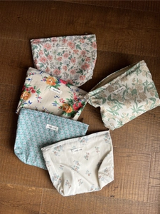 Detailansicht floraler Kosmetiktaschen aus Baumwolle mit Simple Wish Etikett auf Holz