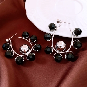 Close-up of geometric silver U-shaped earrings with black faceted beads and a central sphere