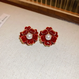 Détail de boucles d'oreilles fleur rouge avec bord doré et perle sur tissu beige