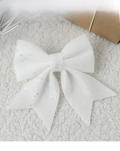 Close-up of a white glitter Christmas bow ornament on soft plush background for decor