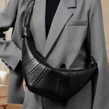 Close-up of black leather croissant bag featuring pleated texture and knot strap detail
