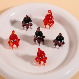 Macro detail of handmade glass octopus pendants in red and purple on a ceramic plate