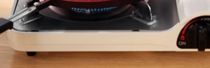Detail of portable gas stove with blue flame and black control knob on a light wood desk