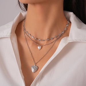 Close-up of three-layer silver necklace with heart pearl and embossed locket pendant