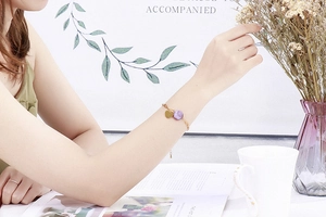 Detail view of a gold heart charm bracelet with purple bead on a woman wrist