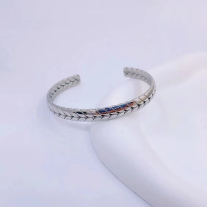 Detailed close-up of C-shaped silver steel bracelet with woven wheat ear texture