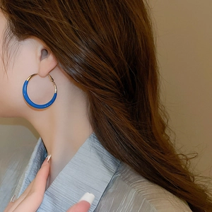 Close-up of minimalist blue enamel hoop earrings worn by a model with brown hair