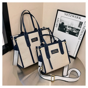 Detail view of two beige canvas tote bags with navy blue leather straps on a metal table