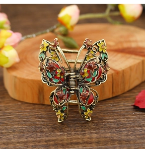 Close-up of vintage butterfly hair claw with colorful floral enamel on a wooden base