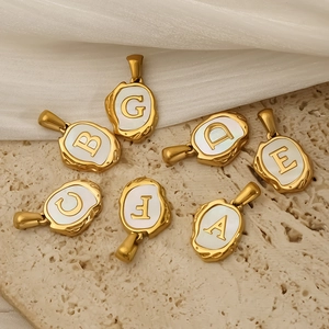 Gold plated stainless steel alphabet pendants with white shell inlay on stone background