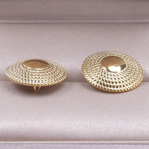 Detail of round gold stainless steel stud earrings with textured relief and polished dome
