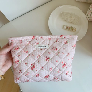 Détail d'une trousse de maquillage rose fleurie matelassée avec étiquette tissée