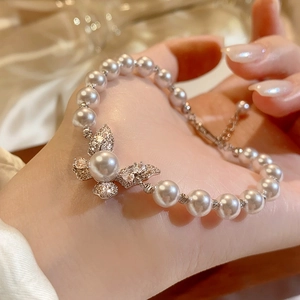 Vista dettagliata di un elegante bracciale di perle con ciondolo a farfalla pavé sulla mano.