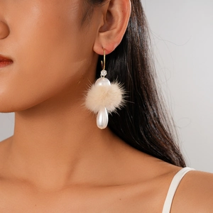 Detailed view of C-shaped gold earrings with beige pompom and white teardrop pearl