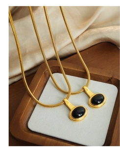 Macro shot of gold snake chain necklace with an oval black gemstone pendant on silk