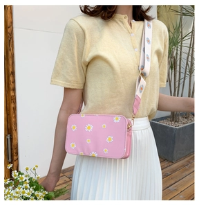 Pink daisy print crossbody bag styled with a white pleated skirt in a sunny outdoor setting