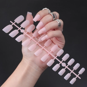 Detail of matte nude pink square fake nails on a stick held against a black background
