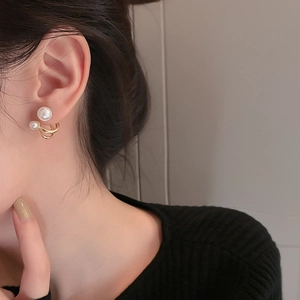 Close-up of elegant C-shaped gold earrings with double pearls worn on female ear