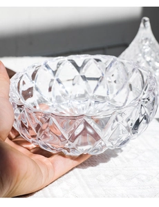 Close-up of a hand holding a geometric diamond-cut glass storage jar with a wavy rim