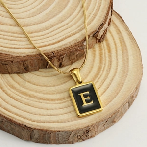 Gold stainless steel snake chain necklace with black enamel letter E pendant on wood