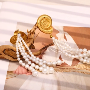 Detail view of gold conch shell earrings with long pearl tassels on a rustic branch