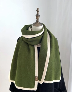 Close-up of olive green knit scarf texture with cream stripes and a small leather brand tag