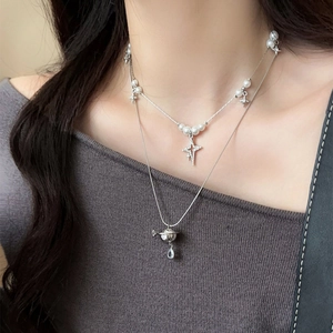 Close-up of layered silver necklace with pearls and sparkling Saturn pendant on model