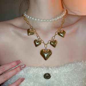 Close-up of layered white pearl choker and gold chain with heart pendants on a model