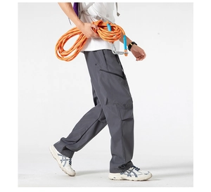 Detail of dark grey cargo pants featuring functional side zippers and adjustable drawstring hems