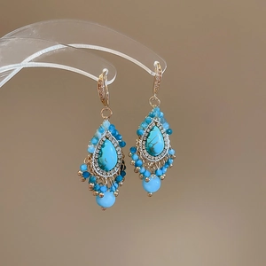 Detail view of turquoise drop earrings with diamond-encrusted accents and blue tassel beads