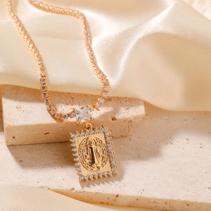 Elegant gold religious pendant necklace with white zircon stones on beige stone background