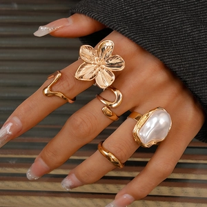 Detail eines fünfteiligen Goldring-Sets mit Blumen und Perlen an einer Modellhand