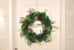 Detail of Christmas wreath with pine cones and red berries featuring a wooden welcome sign